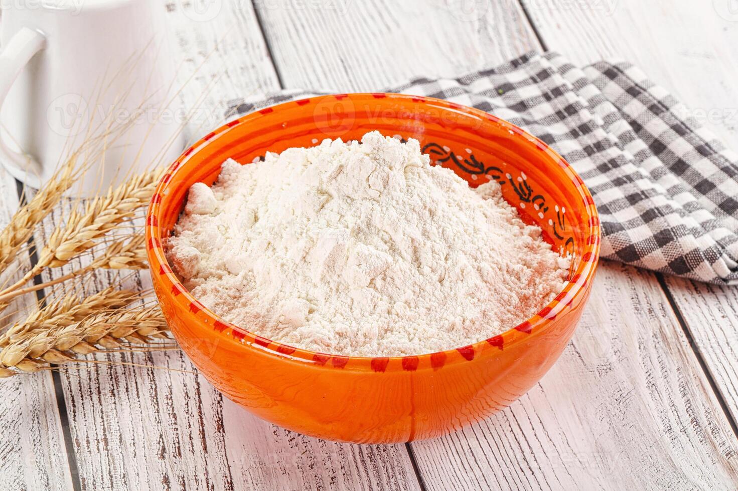 A bowl of flour next to a bowl of milk photo