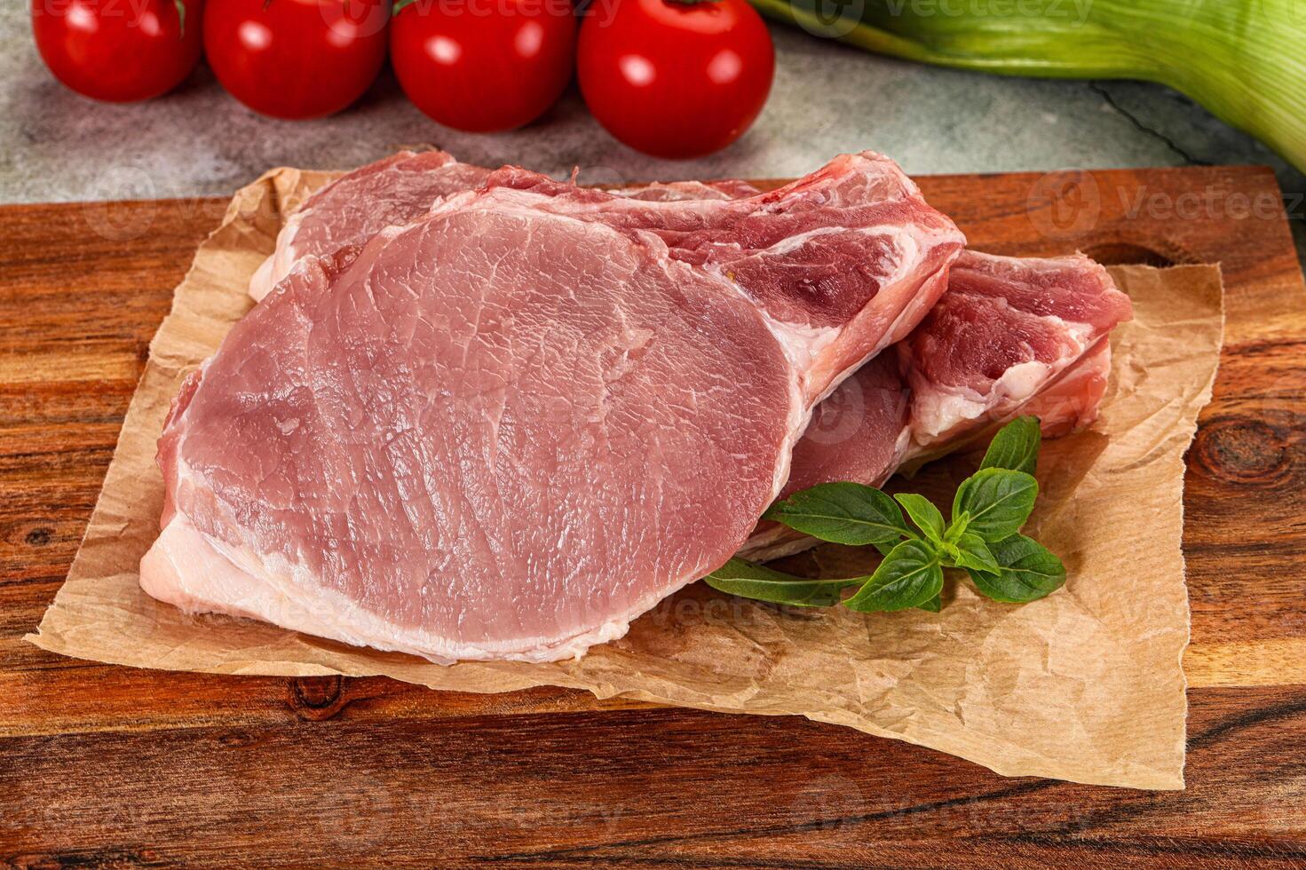 Raw pork chops on a wooden cutting board with tomatoes and herbs photo