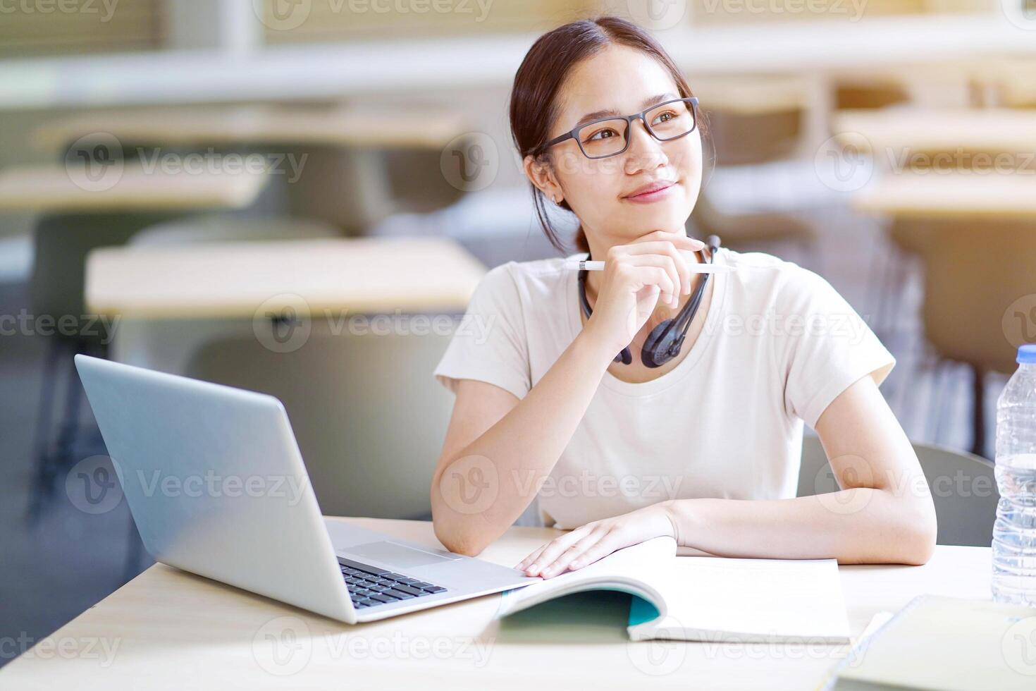Happiness cheerful Asian young female student in casual cloth doing homework with laptop and show a thoughtful face on blurred background. Asian school concept. photo