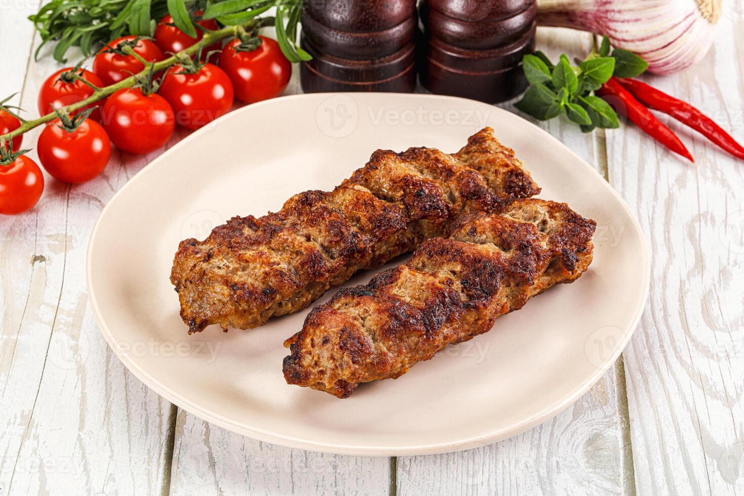 Two meat skewers on a plate with tomatoes and herbs photo