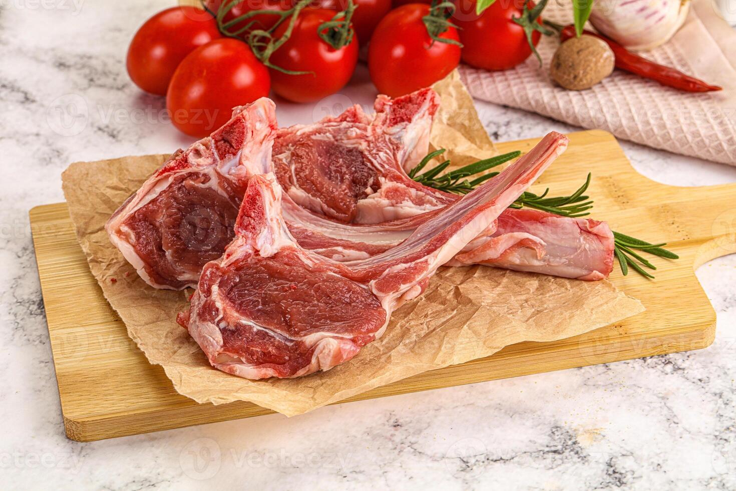 Raw lamb chops on a cutting board with tomatoes and herbs photo