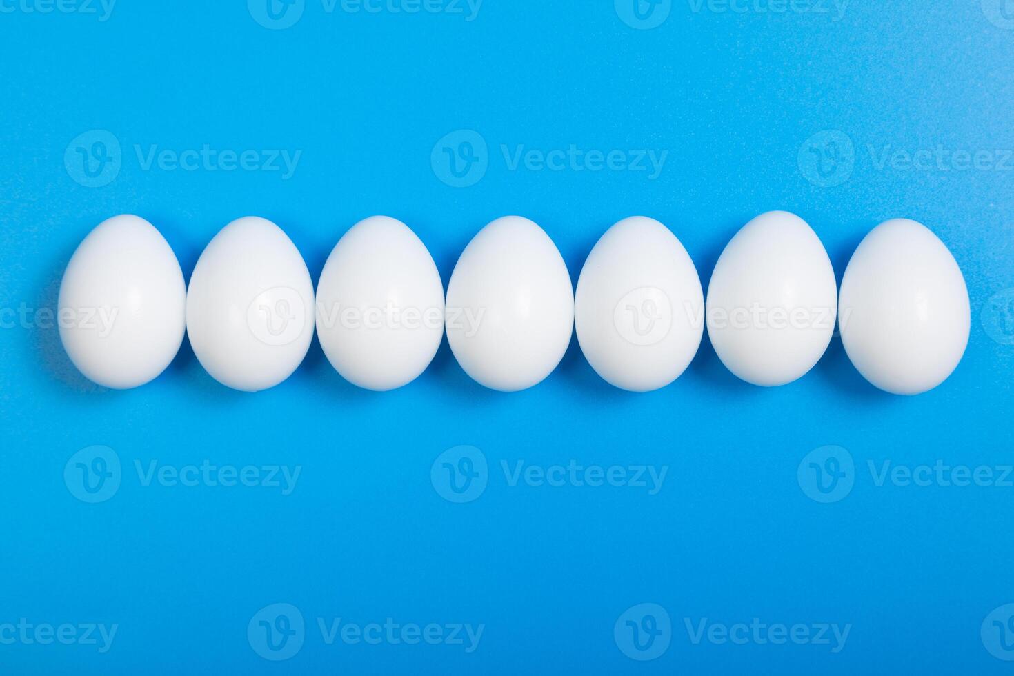 a row of eggs beautifully arranged on a blue background, top view, horizontal format, space for text photo