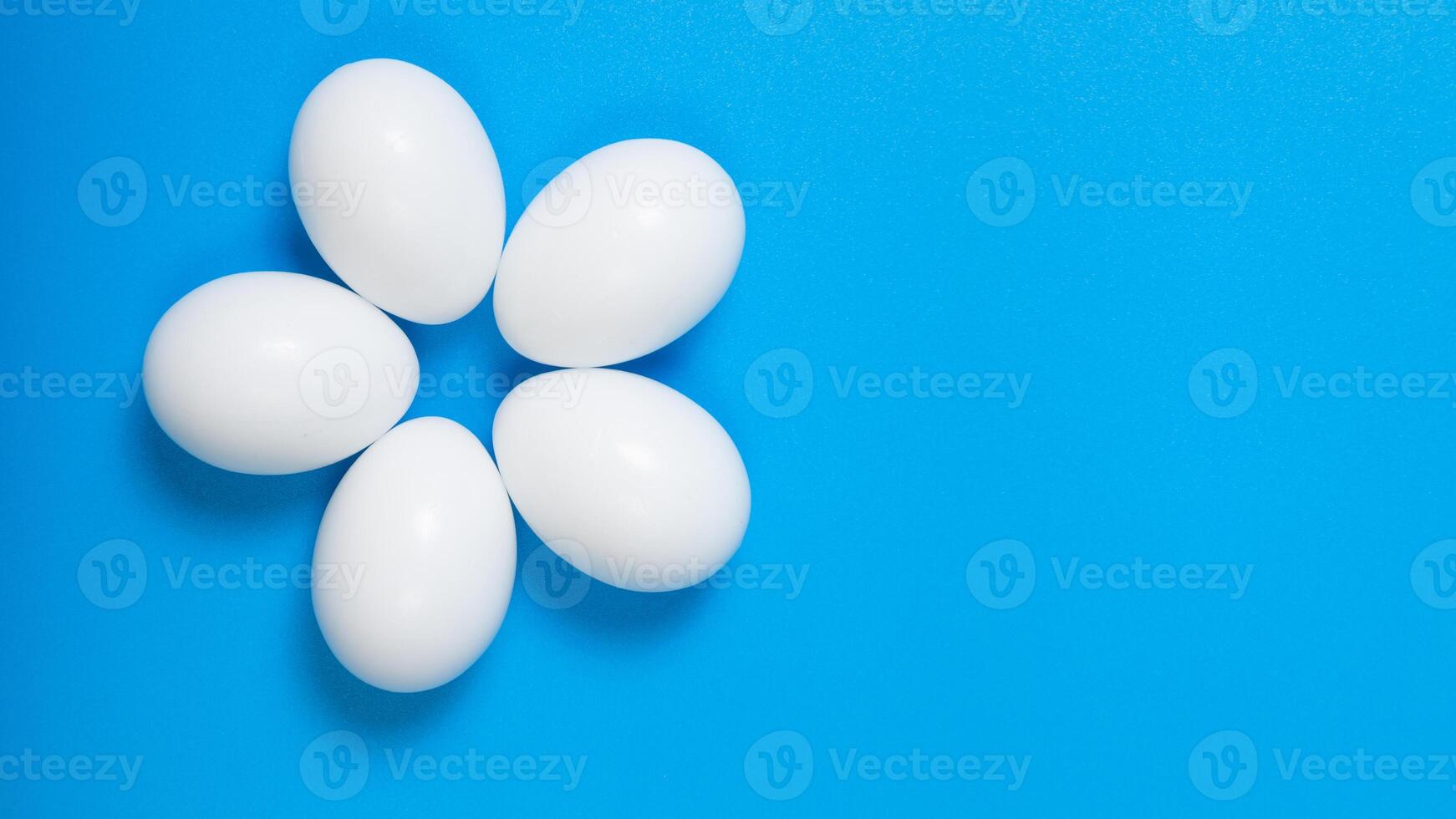 flower-shaped arrangement of white eggs on a blue background, top view, horizontal format, space for text photo
