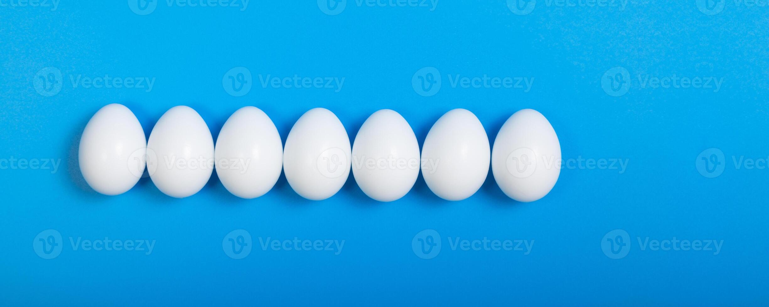 beautifully arranged eggs in a row on a blue background, top view, horizontal format, space for text photo