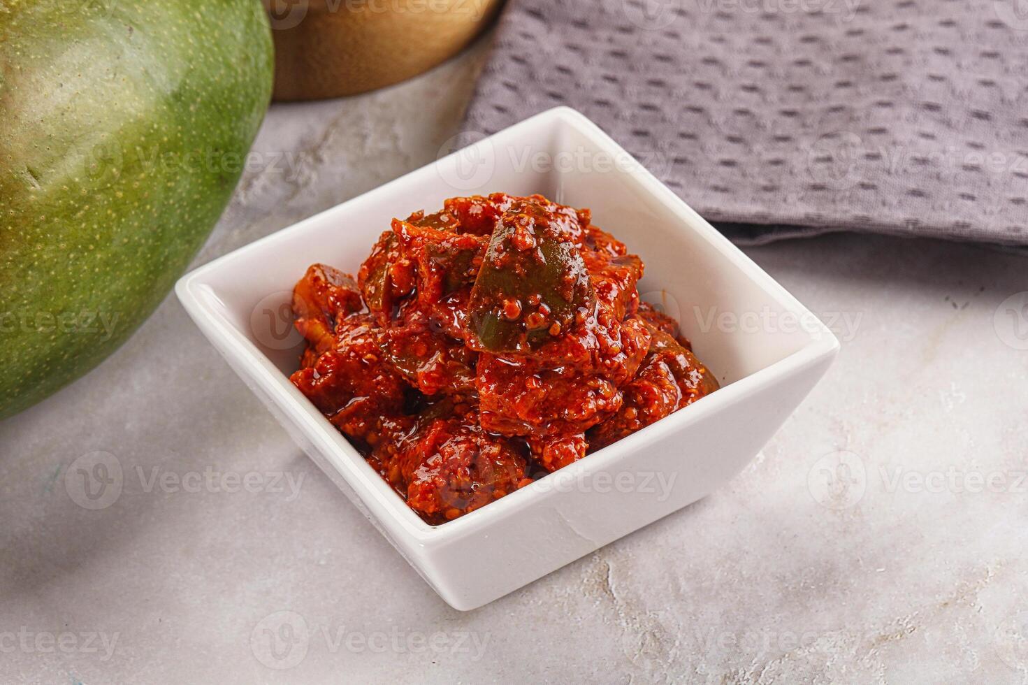A bowl of red sauce next to a large green mango photo