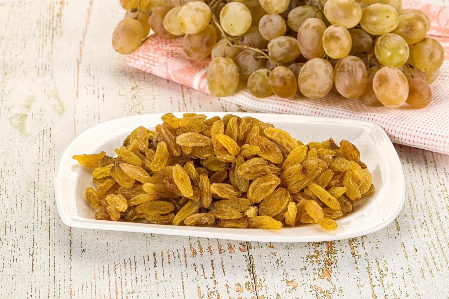 A bowl of raisins and a bunch of grapes on a table photo