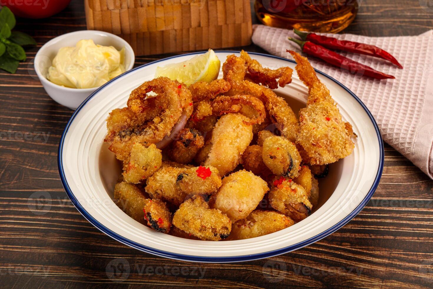 A bowl of fried food on a table next to a bottle of wine photo
