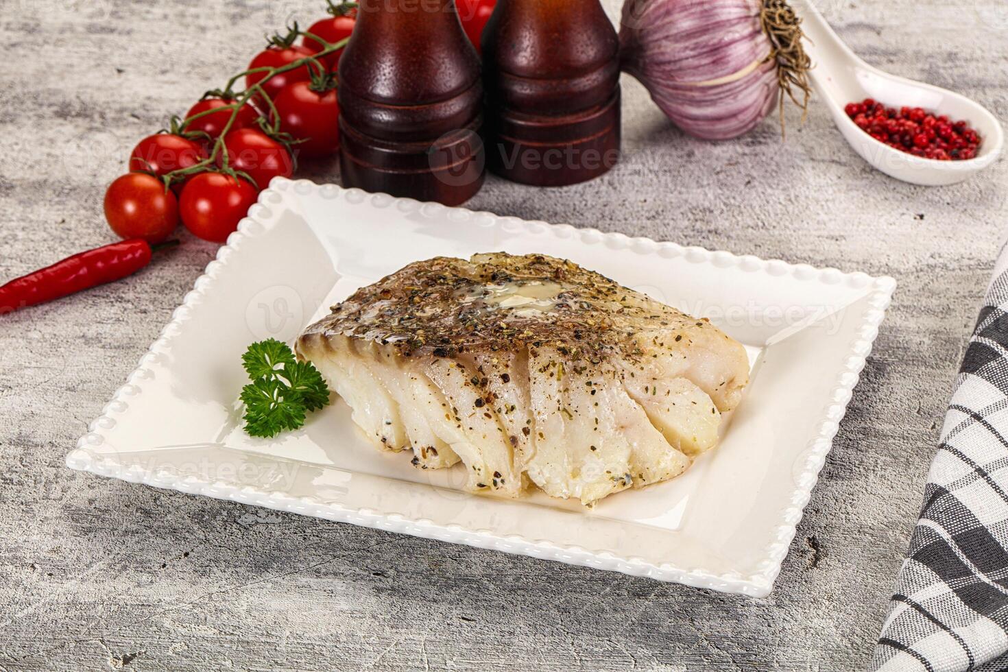 A piece of fish on a white plate with tomatoes and herbs photo