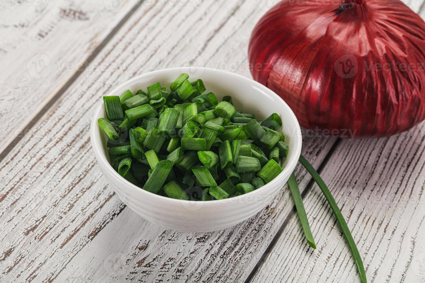 A bowl of chopped green onions and a red onion photo