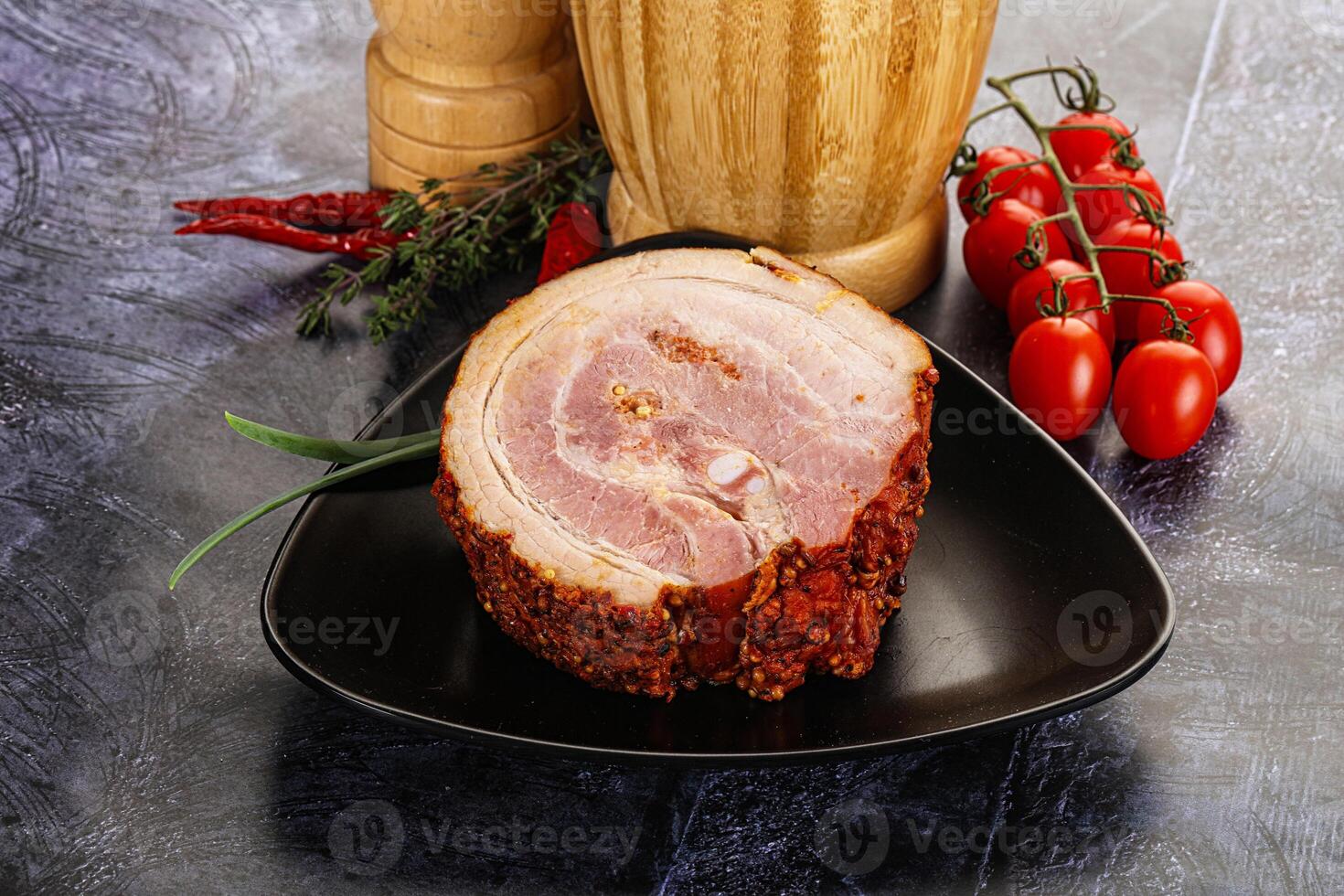 A piece of ham on a black plate with tomatoes and spices photo