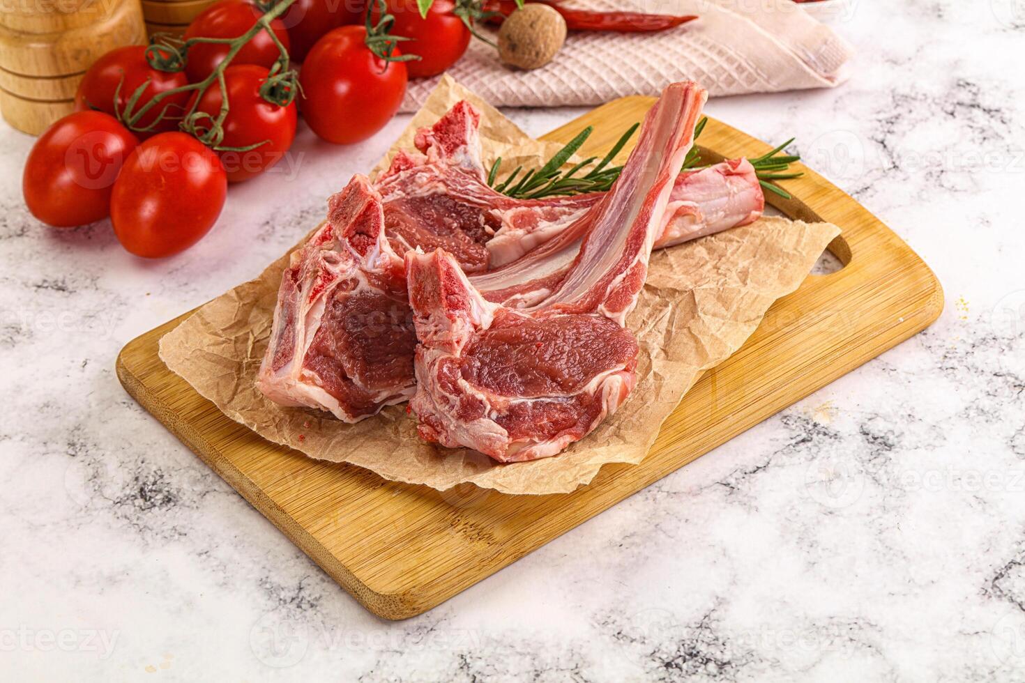 Raw lamb chops on a cutting board with tomatoes photo