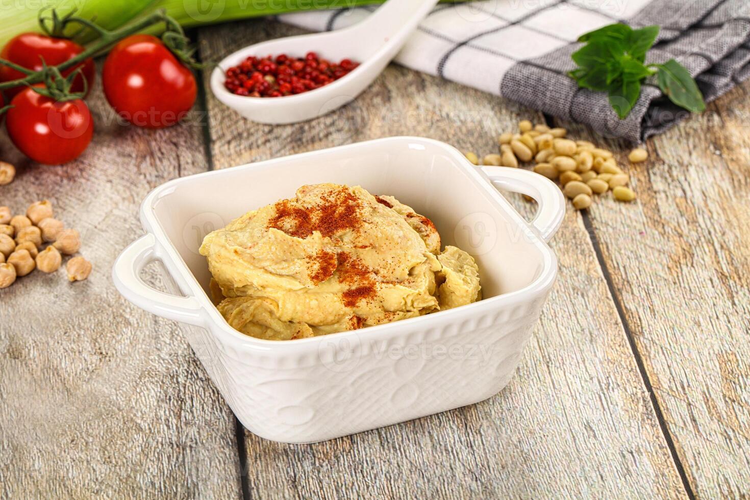 A bowl of hummus with a spoon and a bowl of tomatoes photo