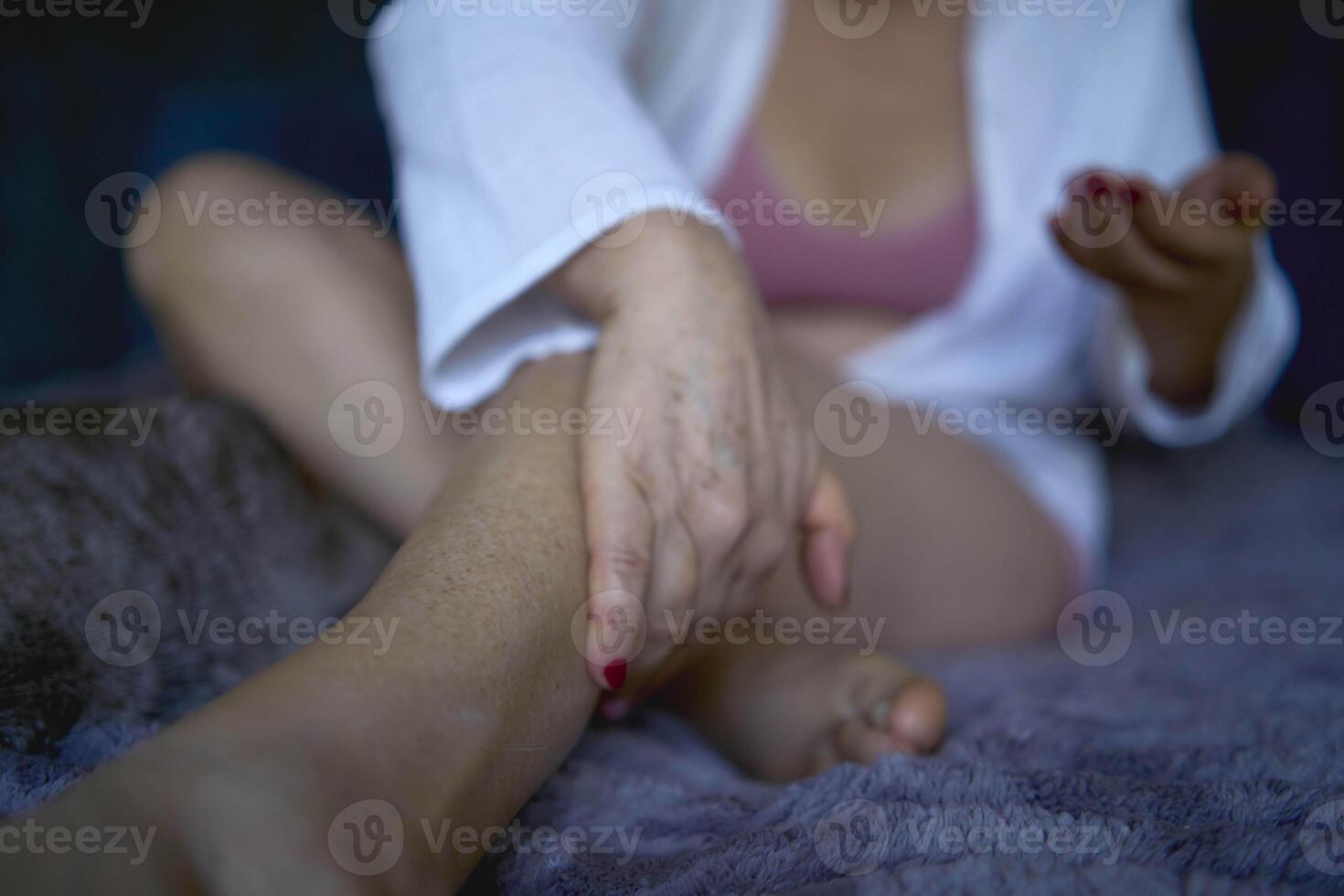 a senior woman in h underwear on the bed performs routine self-care with body cosmetics photo