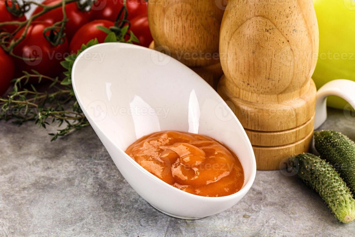 A bowl of tomato sauce next to a pepper and a cucumber photo