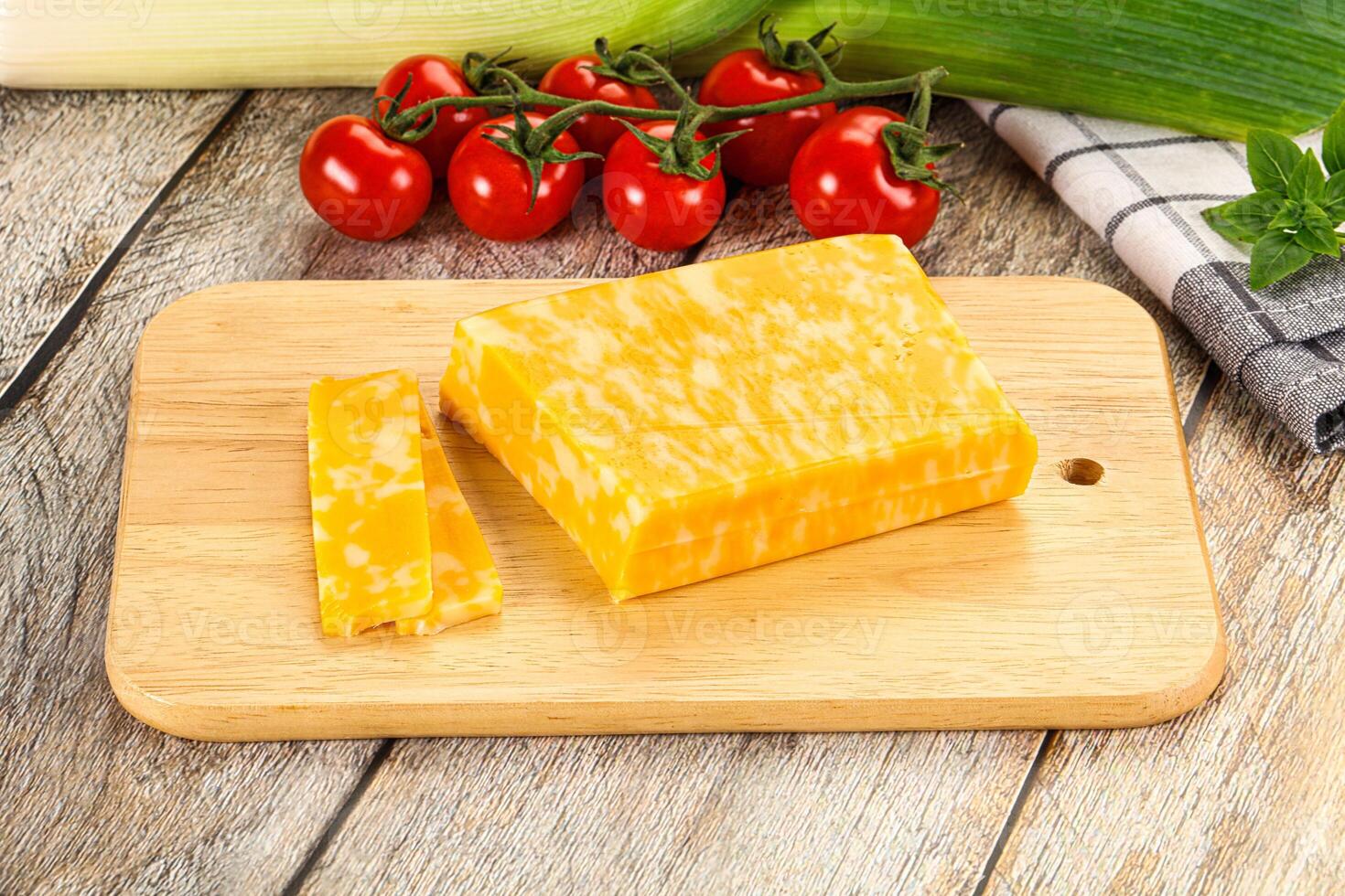 A piece of cheese on a cutting board next to a tomato photo