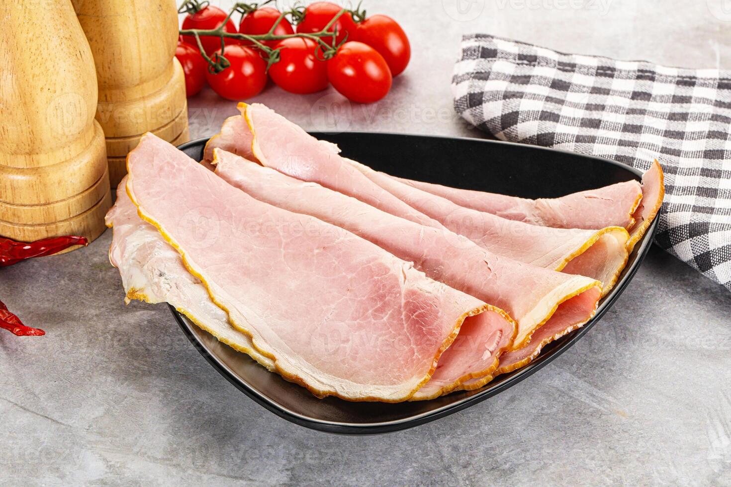 Sliced ham on a black plate with a checkered cloth photo