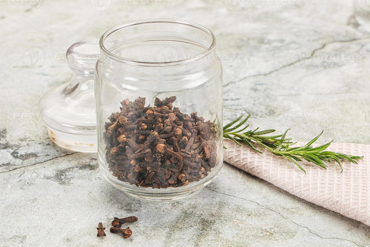 A jar filled with dried spices and a sprig of rosemary photo
