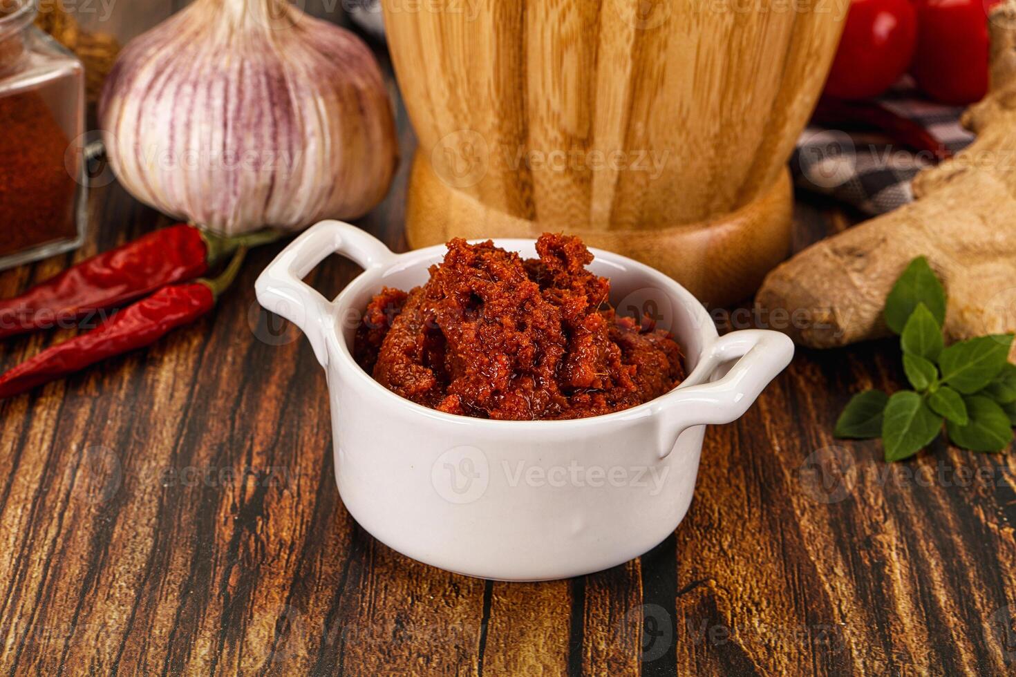 A bowl of chili sauce next to a knife and a pepper photo