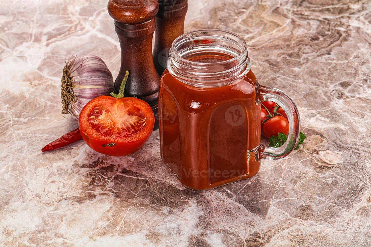 A jar of tomato sauce next to a pepper and a salt shaker photo