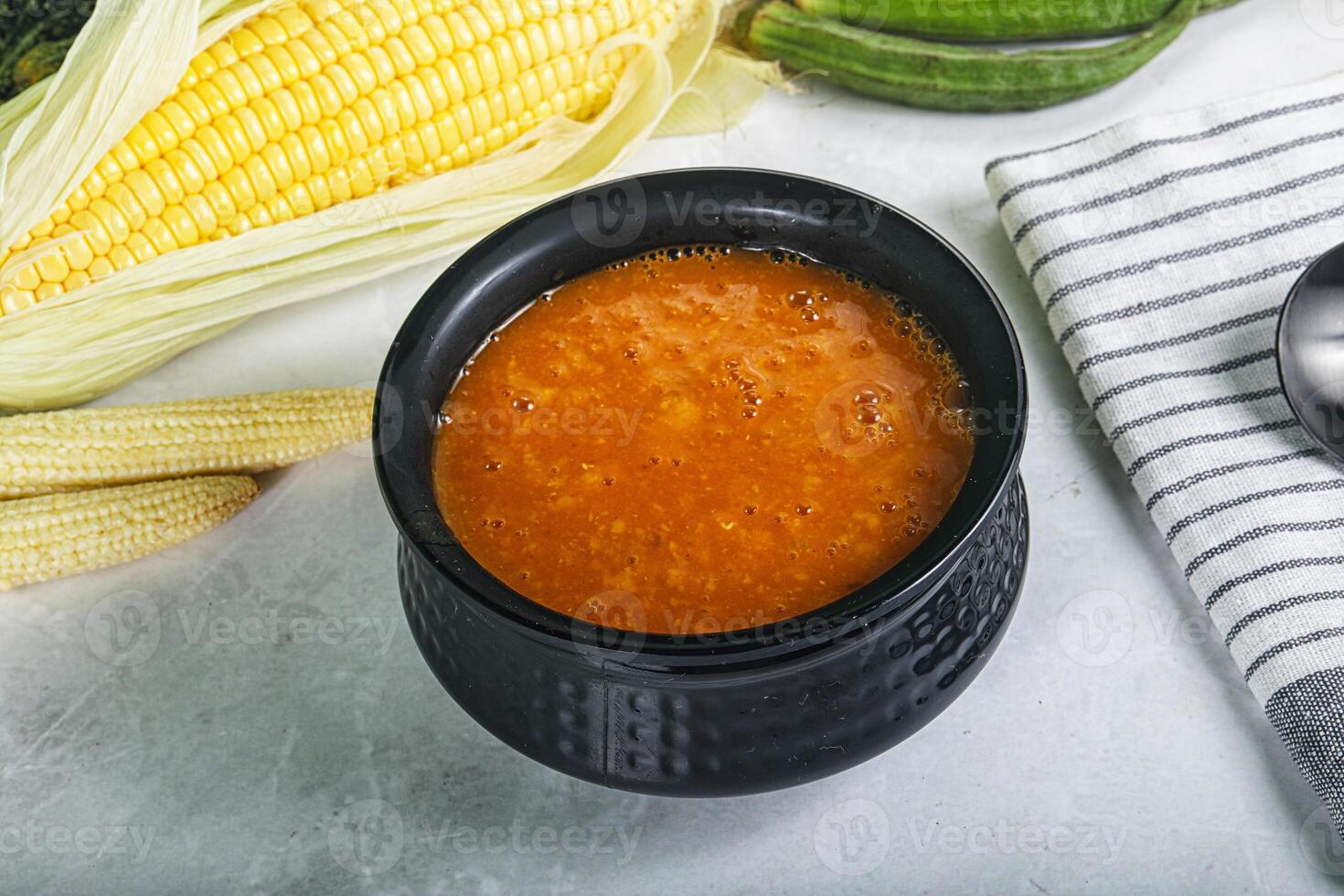 A bowl of soup next to corn and other vegetables photo