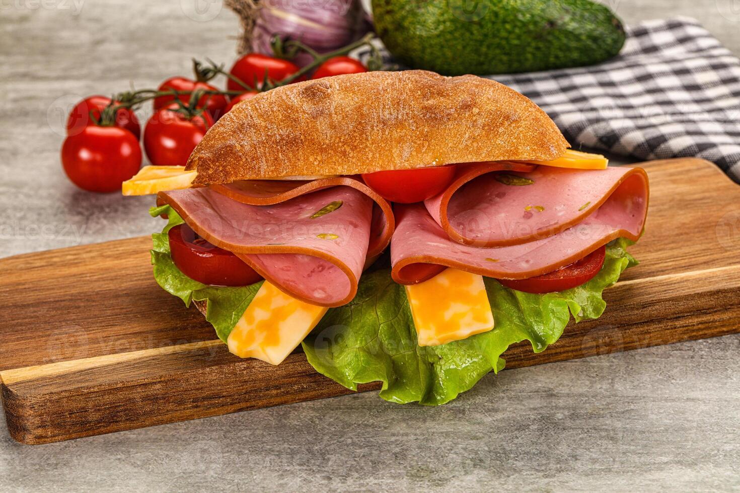 A sandwich with ham, cheese and tomatoes on a wooden cutting board photo