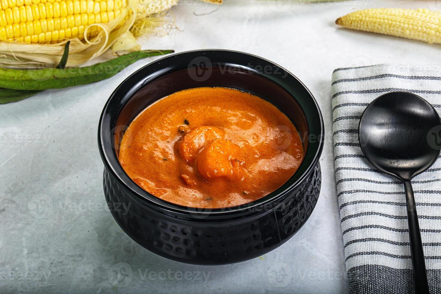 A bowl of soup next to corn and a spoon photo