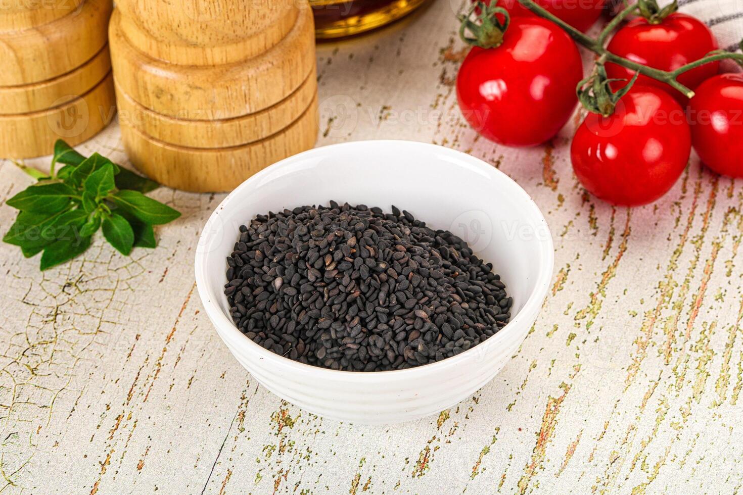 A bowl of black seeds on a table next to tomatoes photo