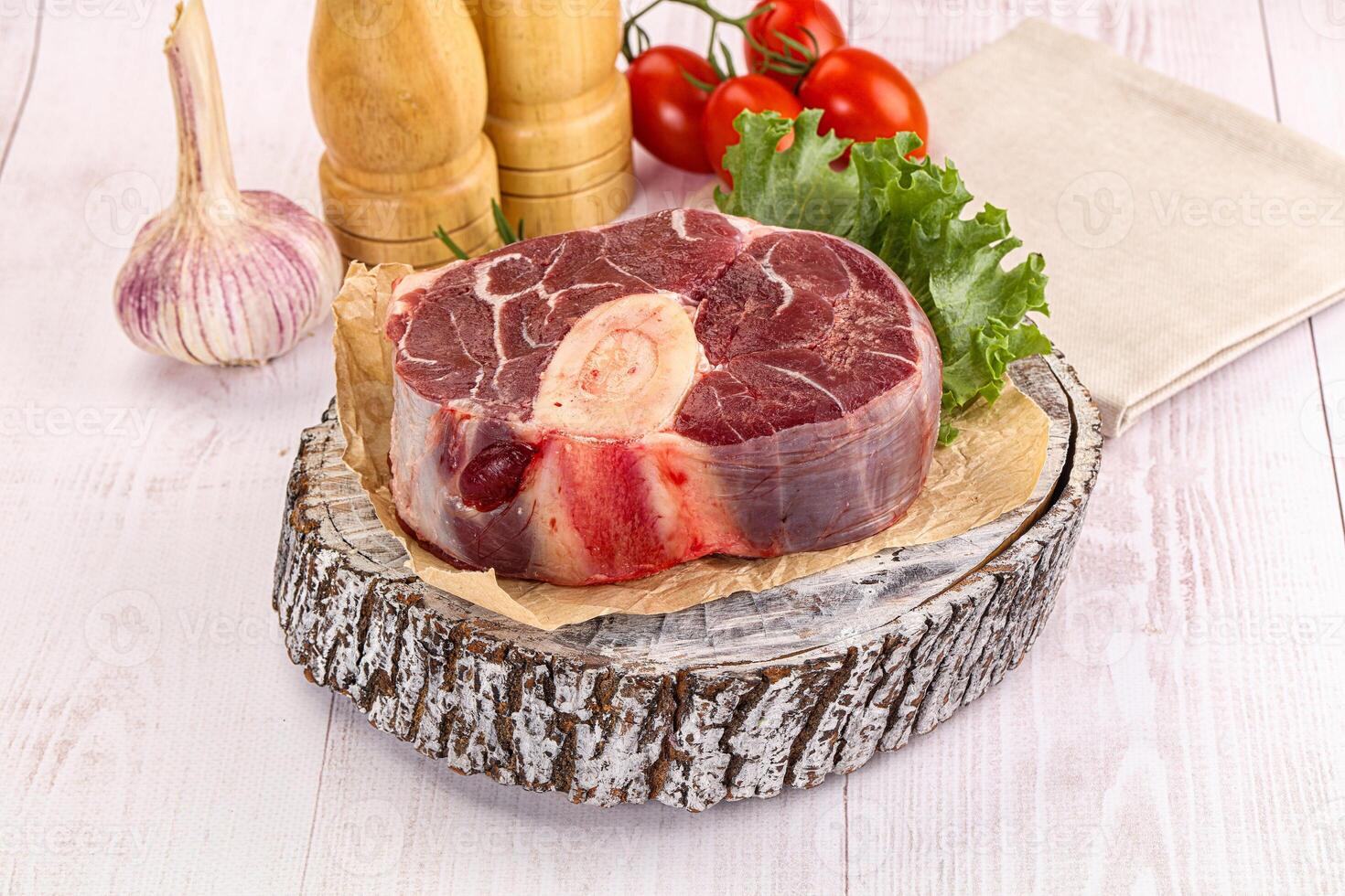 A piece of meat on a wooden table with vegetables and garlic photo