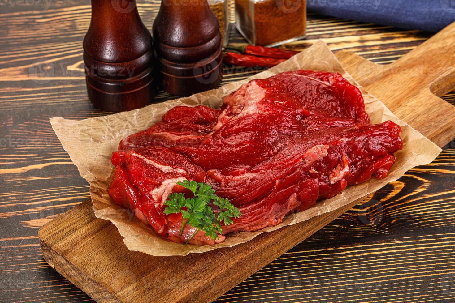 Raw beef on wooden cutting board with spices and condiments photo