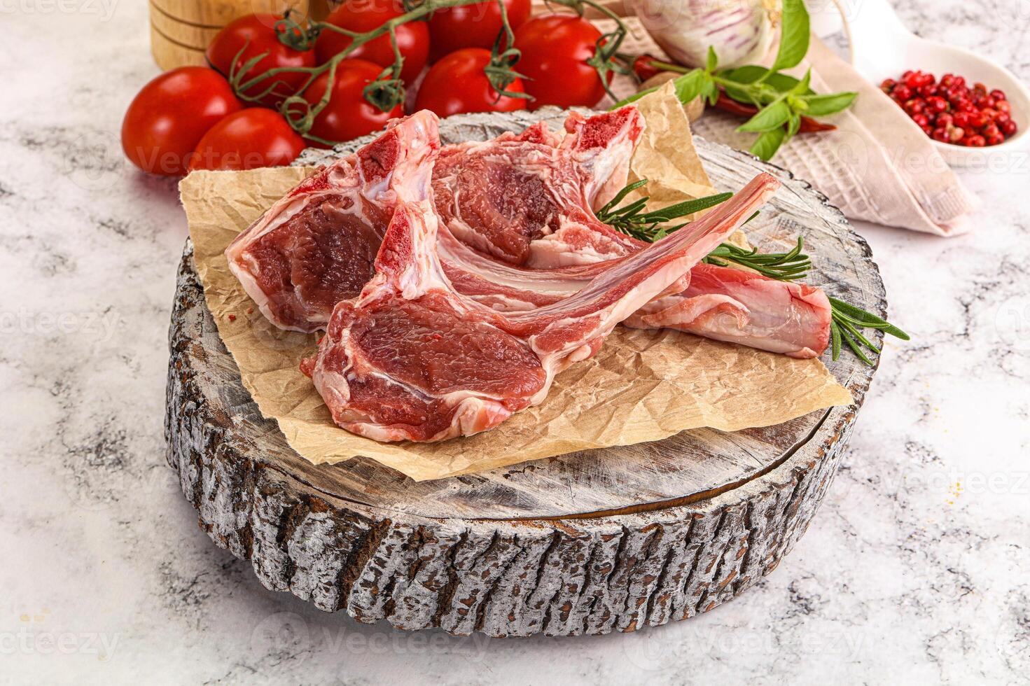 Raw lamb chops on a wooden table with tomatoes and herbs photo