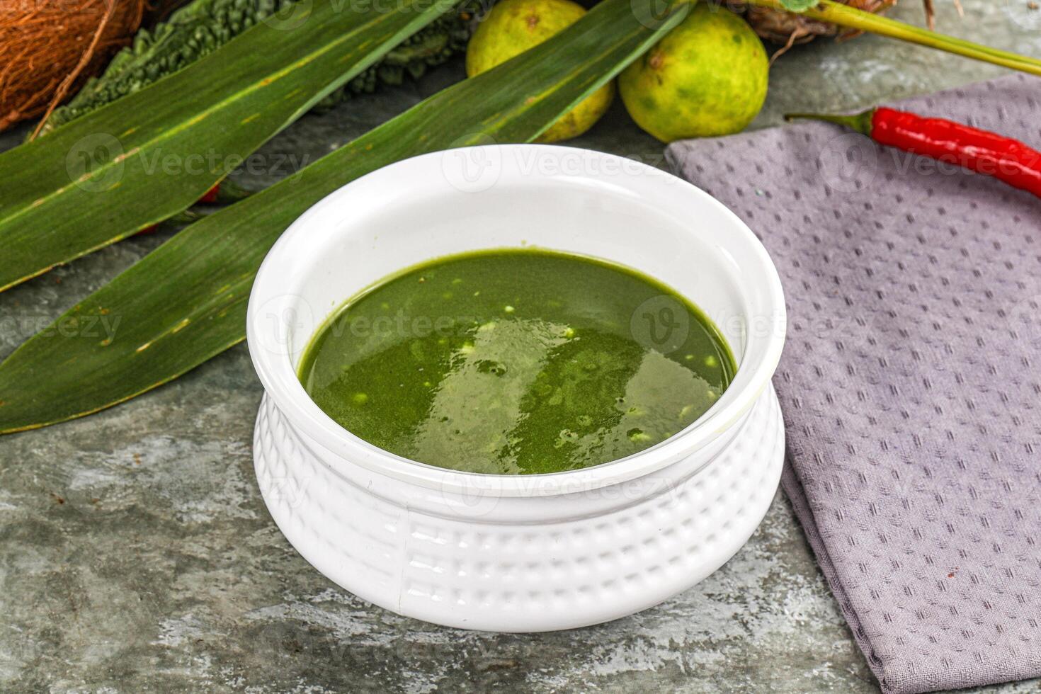 A bowl of green sauce next to some vegetables photo