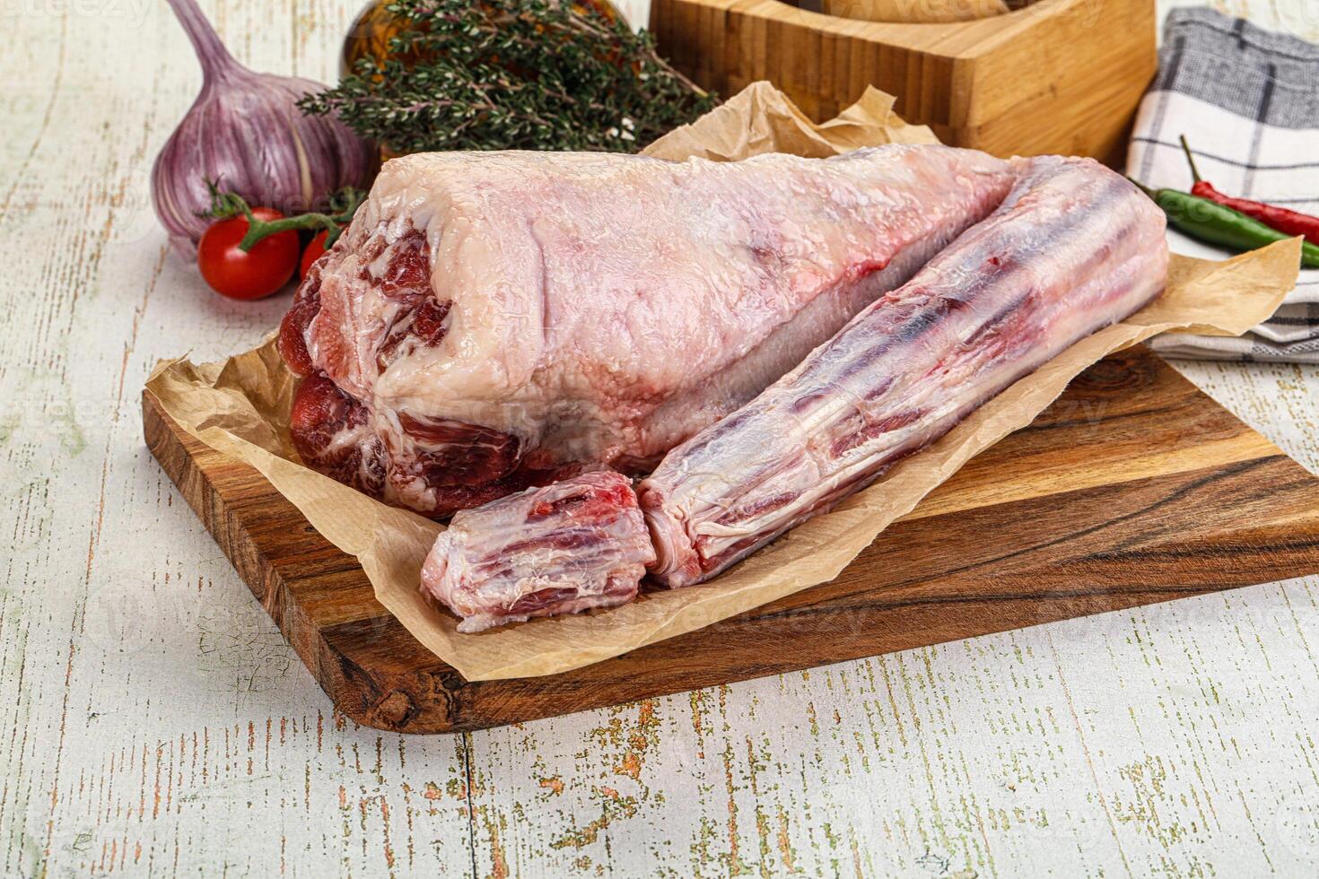A raw lamb leg on a cutting board with a knife and other ingredients photo