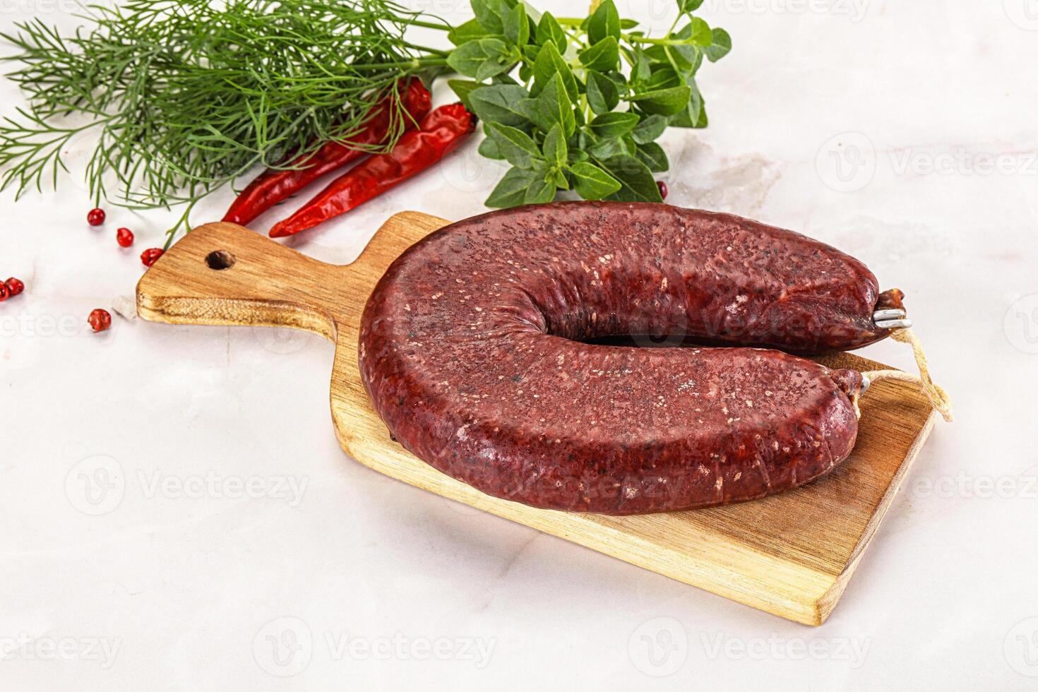 A raw beef sausage on a cutting board with herbs photo