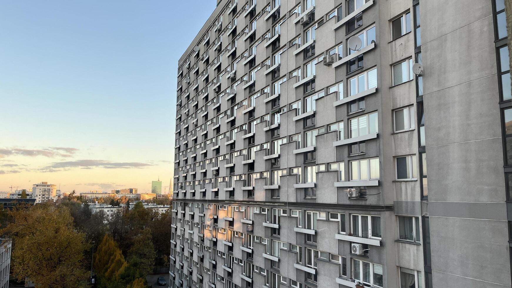 Warsaw, Poland. November 02, 2024. Apartment building with many windows and balconies. The building has a repetitive pattern. A clear blue sky with some clouds, and the sun is set photo