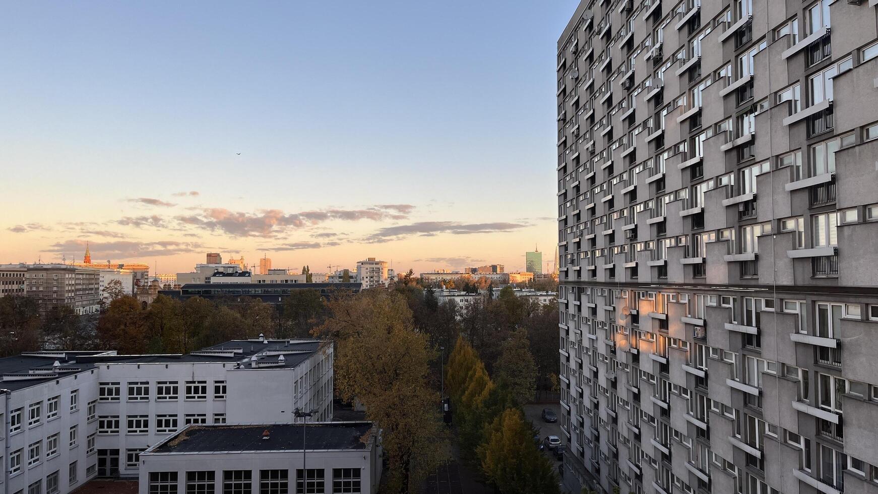 Warsaw, Poland. November 02, 2024. A Gray apartment building with many windows and balconies. The building has a repetitive pattern. A clear blue sky with some clouds, and the sun is set photo