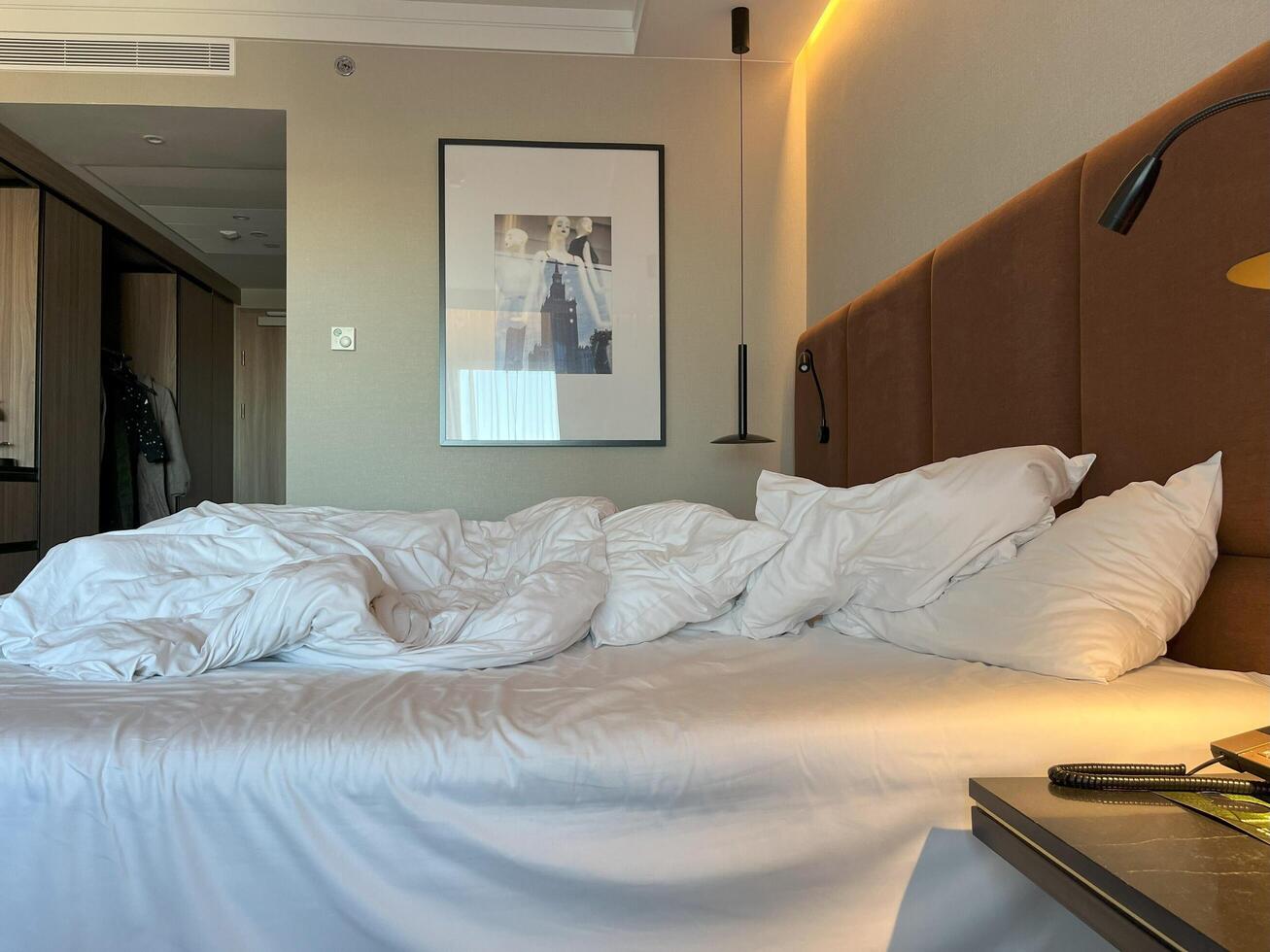 Warsaw, Poland. November 02, 2024. A hotel room with a large bed, a nightstand with a lamp, and a framed picture on the wall. The bed is unmade, with the sheets and pillows rumpled. photo