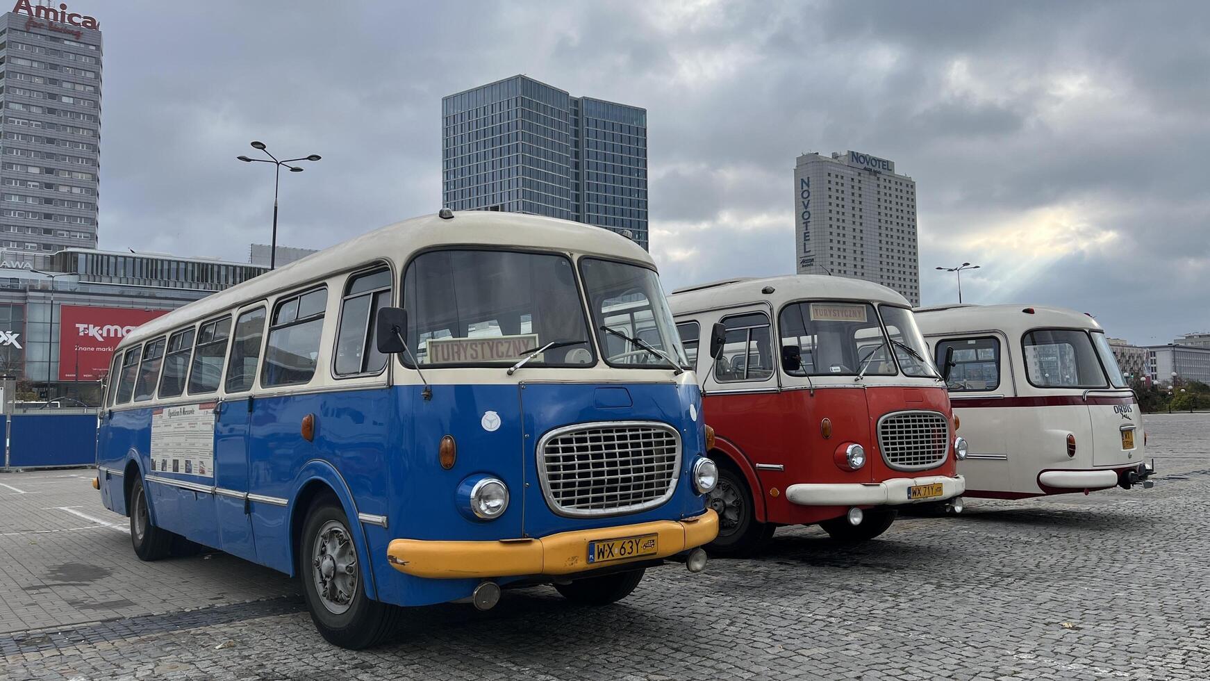 Warsaw, Poland. November 01, 2024. Vintage buses parked in a row in a city setting. The buses are different colors blue, red, and white. They have a classic design with rounded edges and large photo