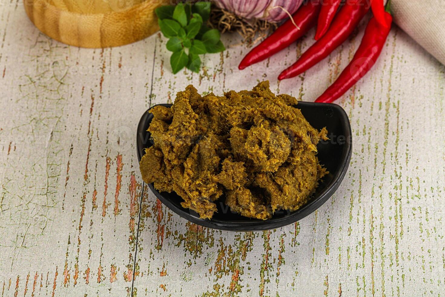 A bowl of curry with spices and herbs on a wooden table photo