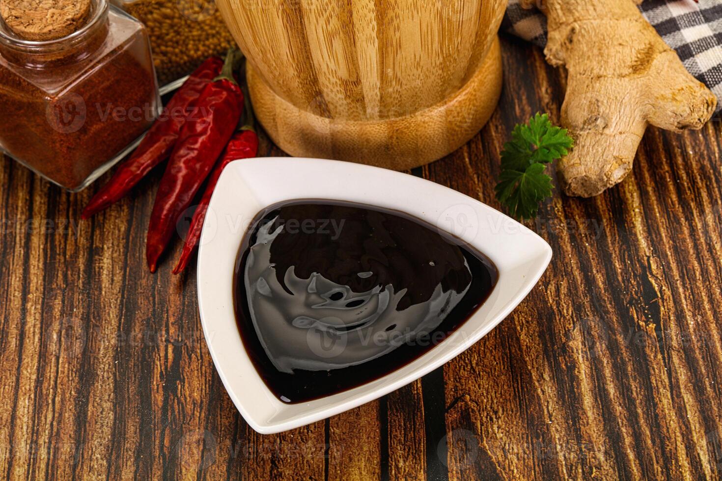 A bowl of black sauce next to spices and ginger photo
