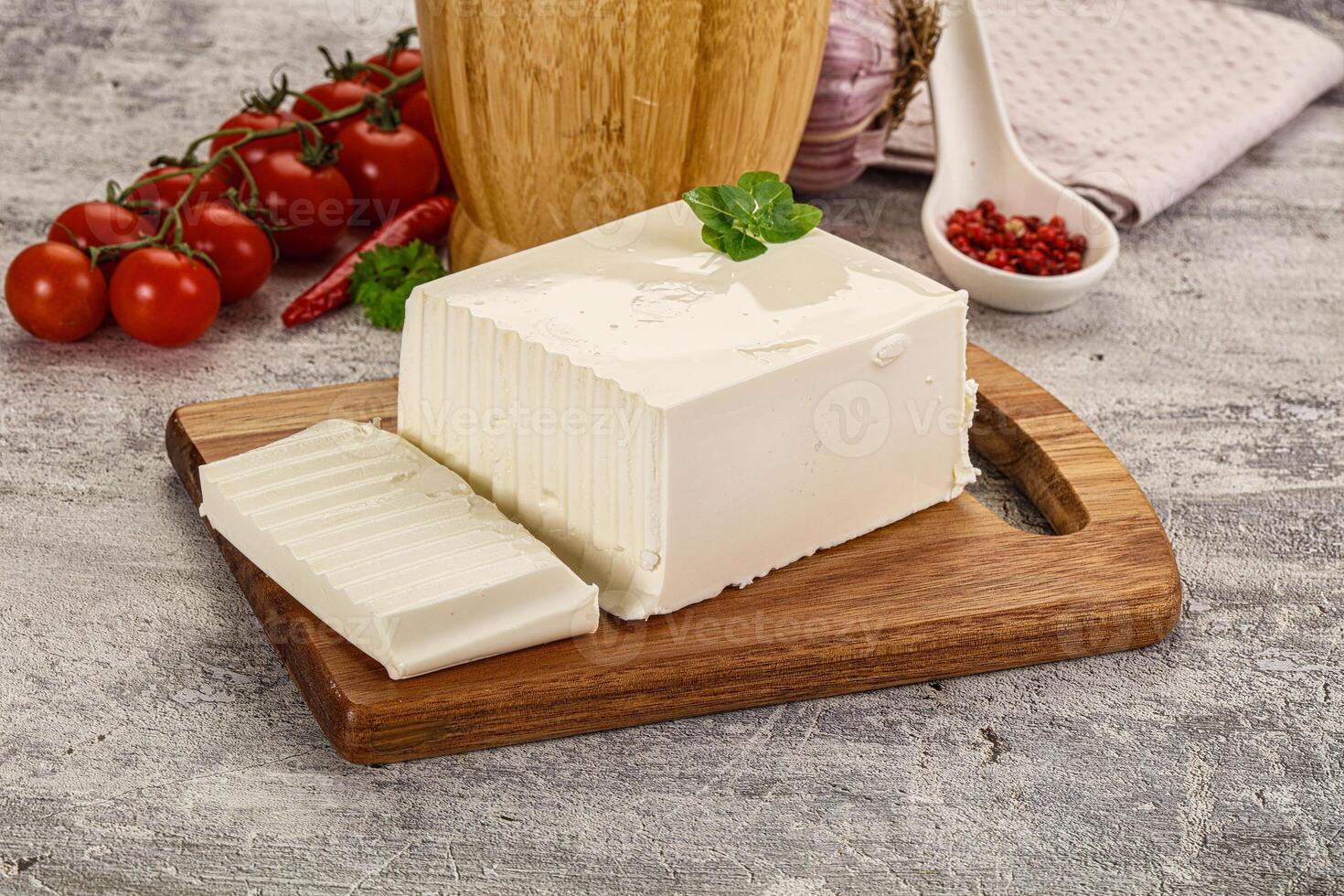 A piece of cheese on a cutting board next to tomatoes and a wooden cutting board photo