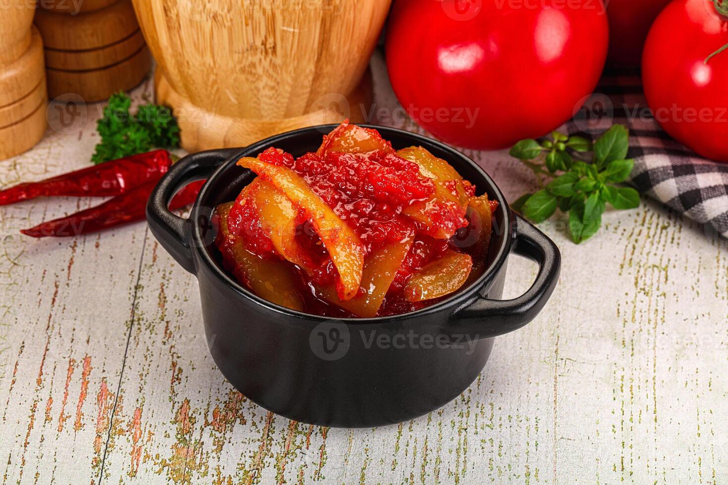 A black pot with tomatoes and peppers sitting on a table photo