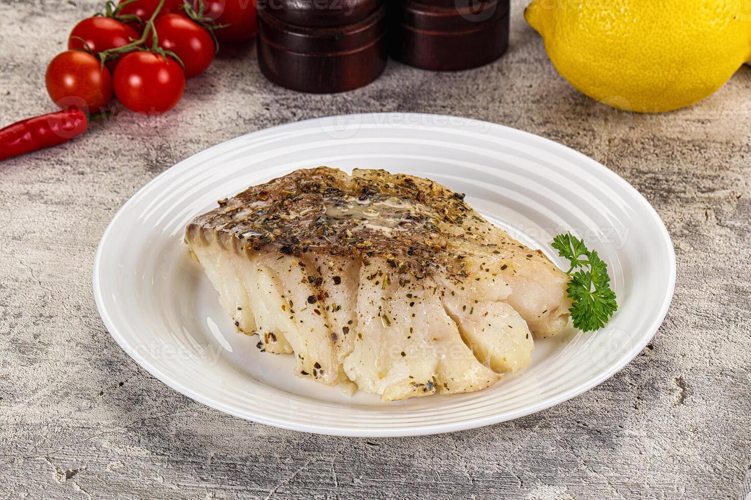 A piece of fish on a white plate with lemon and herbs photo