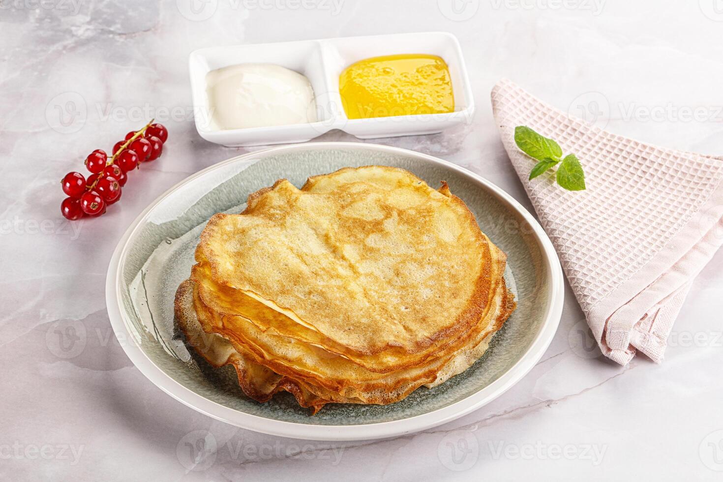 A stack of pancakes on a plate with a bowl of sauce and a bowl of yogurt photo