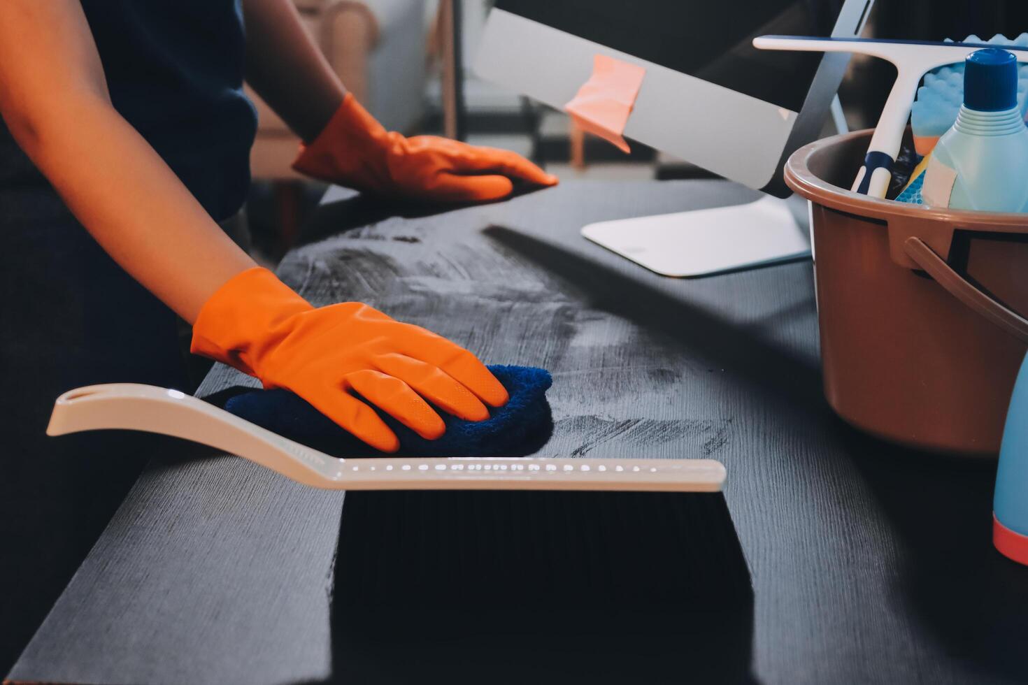 A woman wearing gloves and an orange rubber glove is cleaning a desk photo
