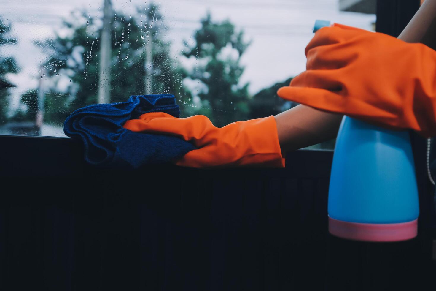 A person wearing an orange glove and rubber gloves is cleaning a window photo