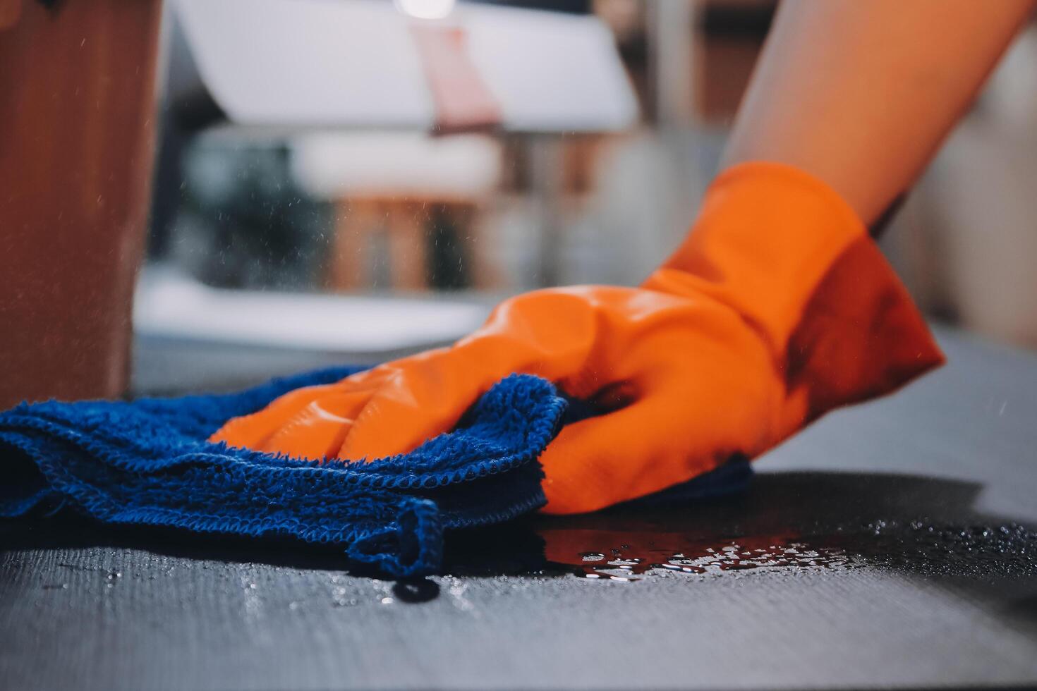 A person wearing an orange glove cleaning a table photo