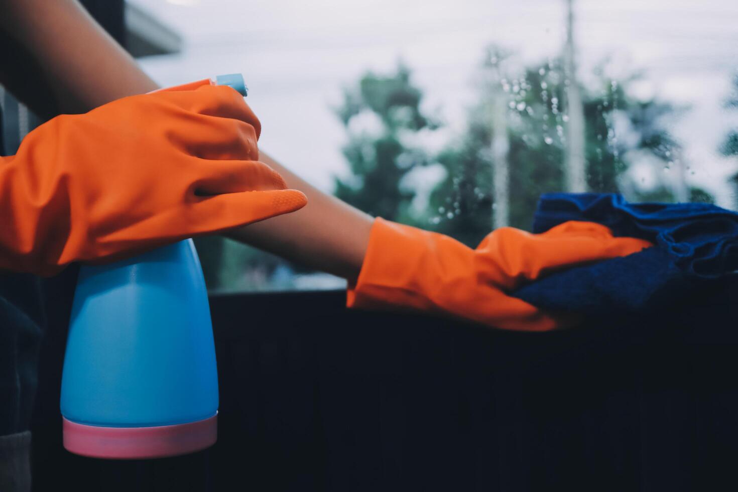 A person wearing an orange glove and rubber gloves is cleaning a window photo