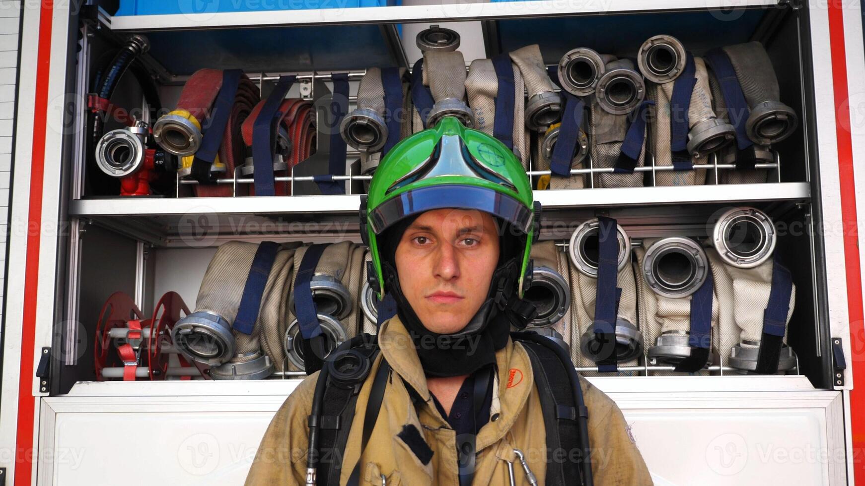 Portrait of tired male firefighter standing near a fire engine. Young fireman in protective uniform posing against the background of big red truck. Concept of saving lives and heroic profession photo
