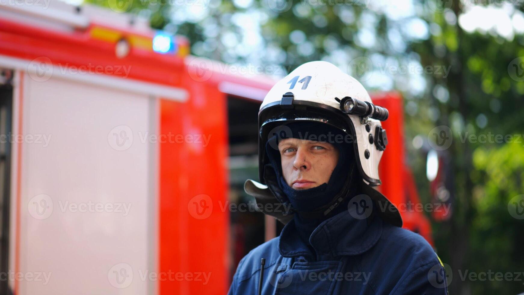 Portrait of confident male fireguard with dirty face standing near a fire engine. Young fireman in full equipment posing after fire against the background of big red truck. Concept of saving lives photo
