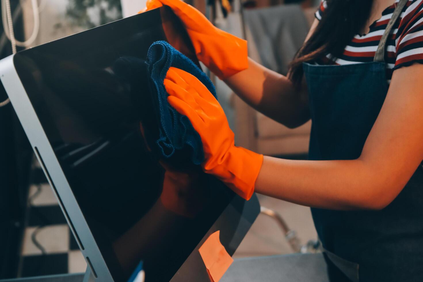 A woman wearing orange gloves and an apron is cleaning a computer photo